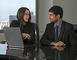 man and woman discussing at a desk with laptop. Many of Assessability's clients are happy to speak to colleagues in their profession about our work as an expert witness and care cost consultant.
